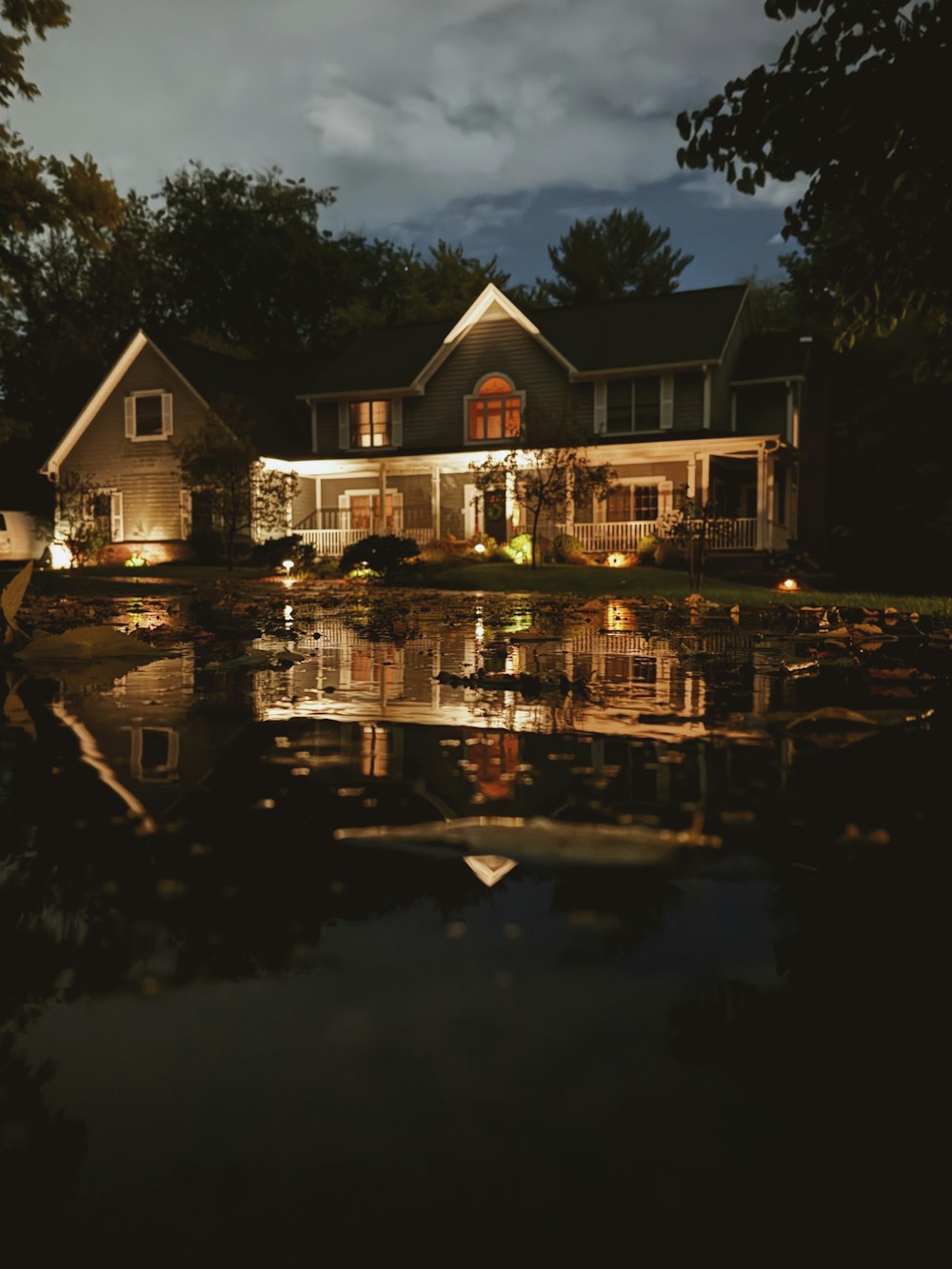 a house is lit up at night with a pond in front of it