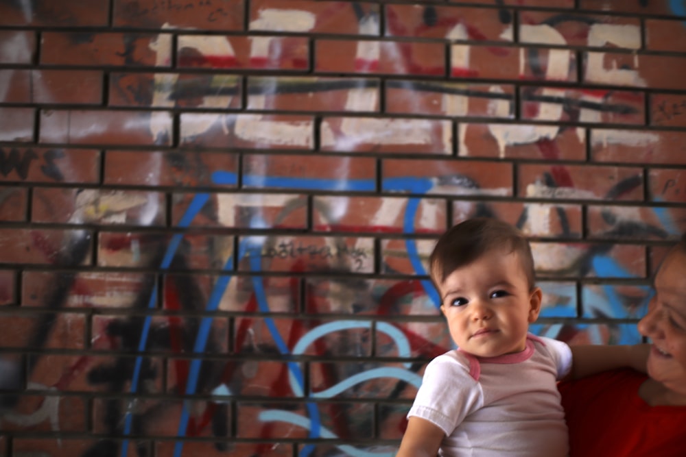 a woman holding a baby in front of a brick wall