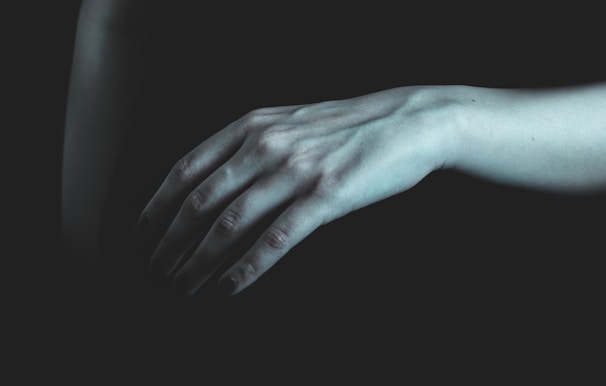 Close-up of a delicate hand tracing faint patterns on a glossy black surface, bathed in deep blood-red light.