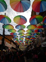 A vibrant street scene showing people engaging with local newsstands under colorful umbrellas.
