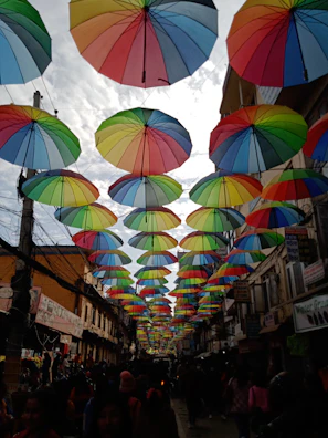 A bustling city street scene with people walking under colorful umbrellas.