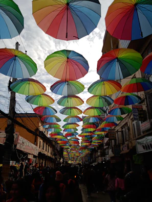 A vibrant street scene showing people engaging with local newsstands under colorful umbrellas.