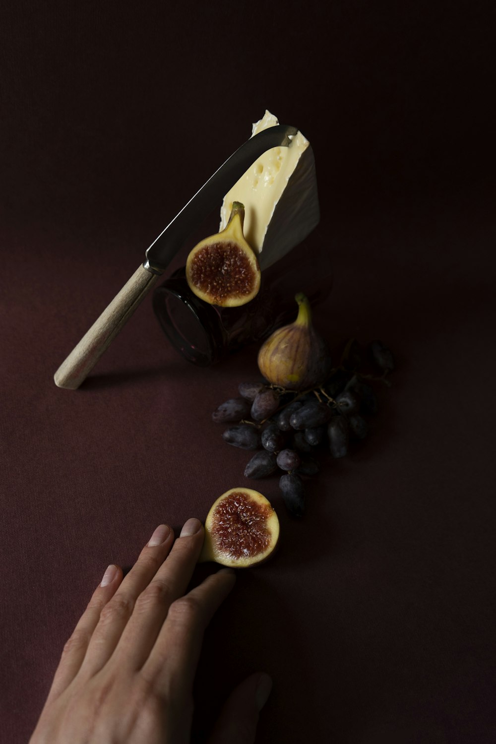 a hand reaching for a piece of cheese next to figs and grapes