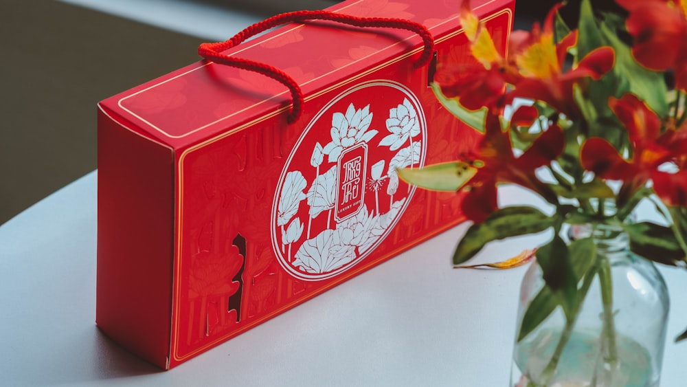 a vase with flowers and a red box on a table