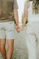 a man and a woman holding hands walking down a road