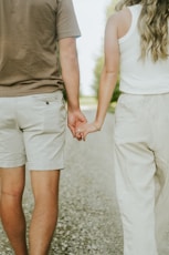 a man and a woman holding hands walking down a road