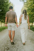 A wide shot of the couple walking hand in hand down a tree-lined path.