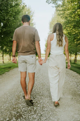 A wide shot of the couple walking hand in hand down a tree-lined path.