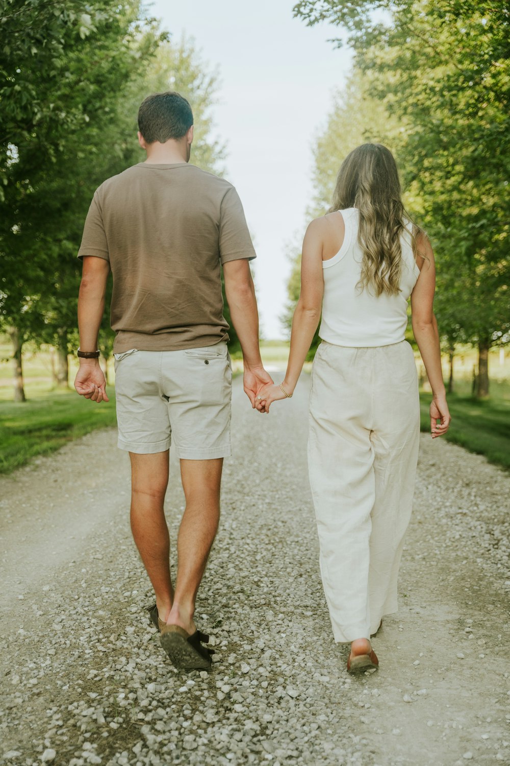 a man and woman walking down a dirt road holding hands