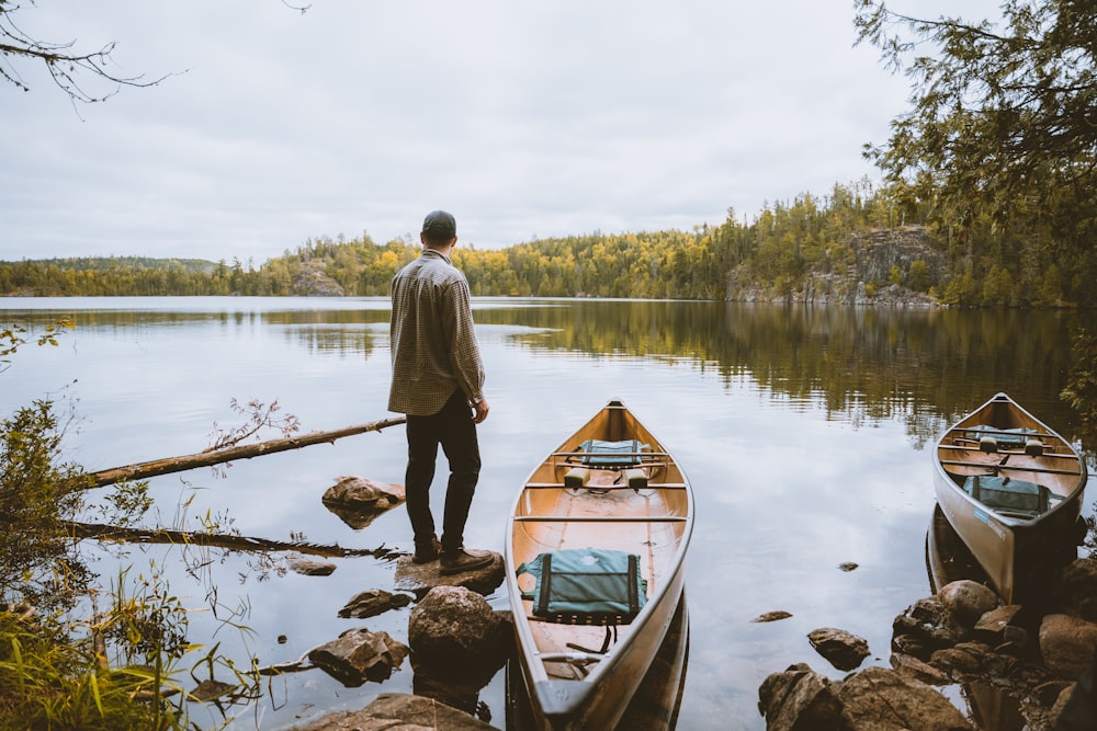 a man standing on a rock next to two canoes