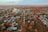 An aerial view of a residential area featuring a grid of streets and houses. The landscape is richly colored with autumn foliage, as trees in shades of red, orange, and brown scatter throughout the neighborhood. A large industrial building, possibly a grain silo, stands prominently.