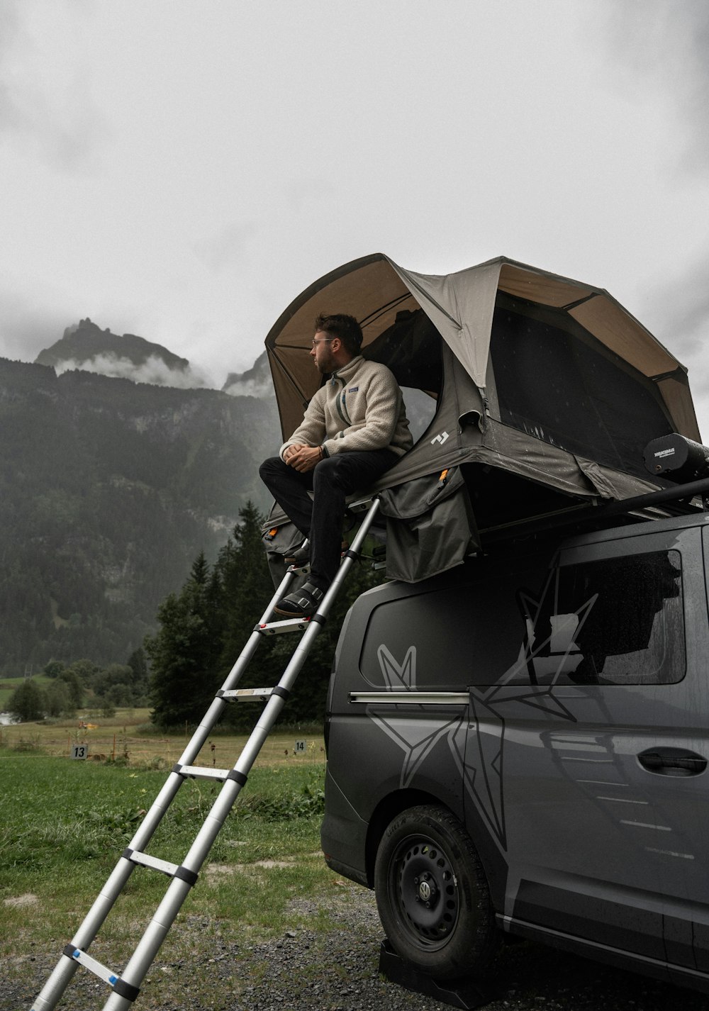 a man sitting on top of a ladder next to a van