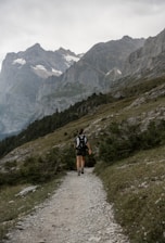 A traveler trekking along a lush green mountain trail in the Indian Himalayas.
