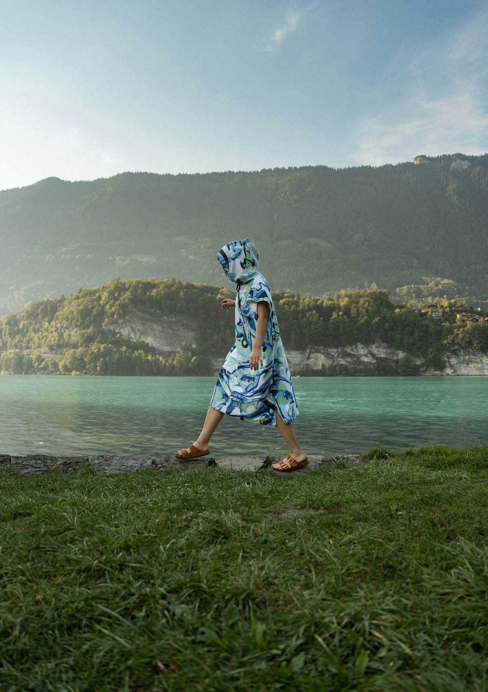 a woman walking across a lush green field next to a lake