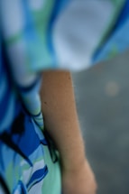 A close-up view of a person's arm wearing a garment with a colorful, abstract pattern. The fabric features shades of blue, green, and hints of white and black, creating a vibrant, flowing design. The focus is on the arm and the fabric, with a soft, blurred background.