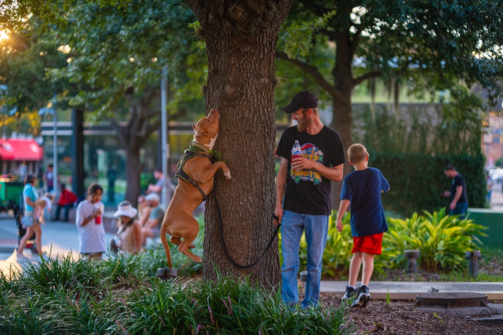 a man standing next to a tree with a dog on a leash