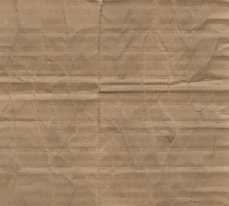 A textured surface characterized by horizontal and vertical creases and folds on brown cardboard material.