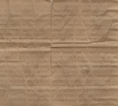 A textured surface characterized by horizontal and vertical creases and folds on brown cardboard material.