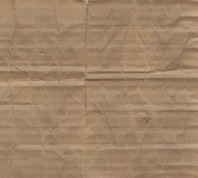 A textured surface characterized by horizontal and vertical creases and folds on brown cardboard material.