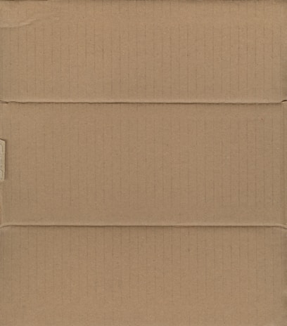 A brown cardboard box, closed and laid flat, with visible creases and slight shadows indicating the box's structure with its intersecting flaps.
