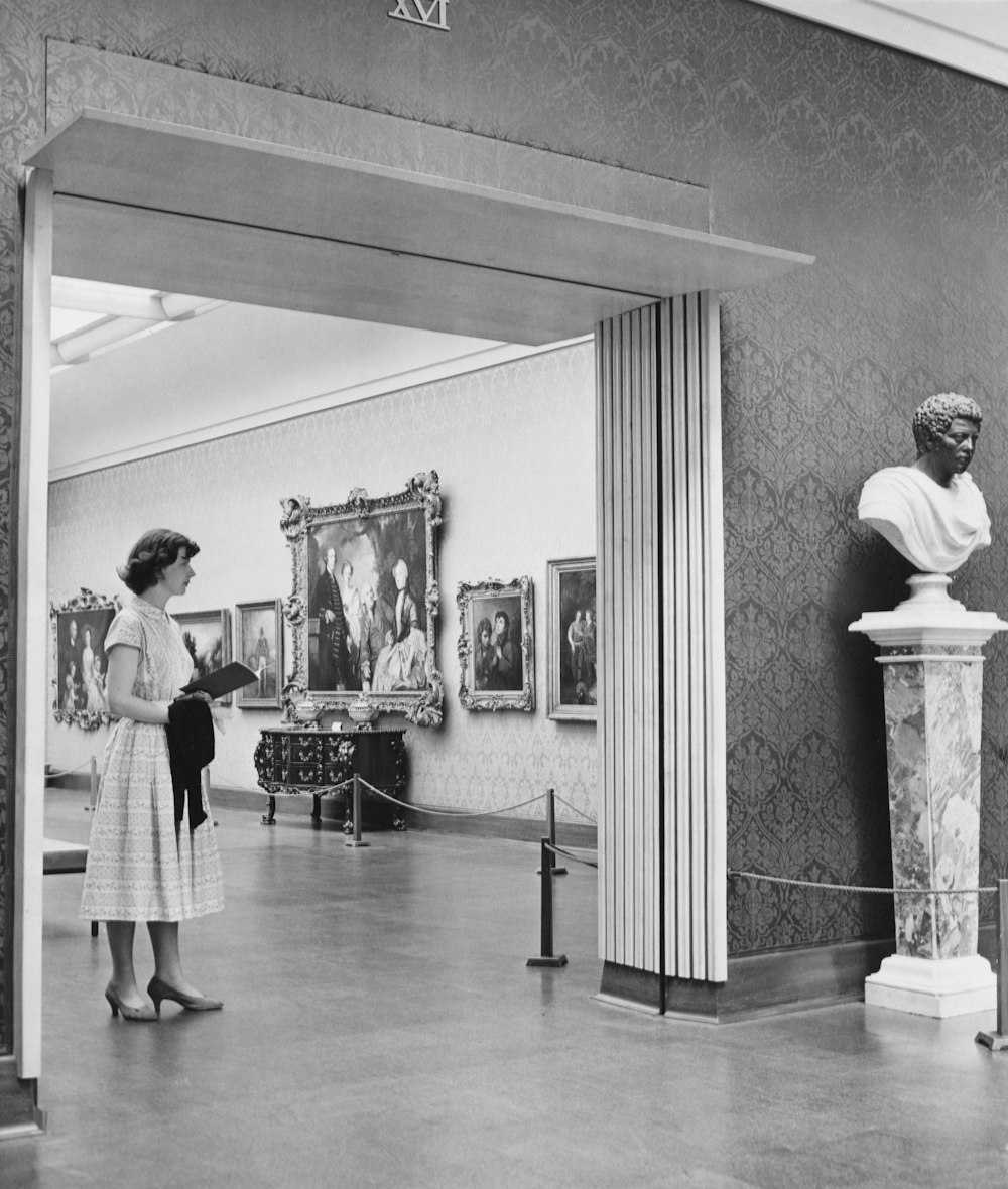 a woman standing in a museum looking at a busturine