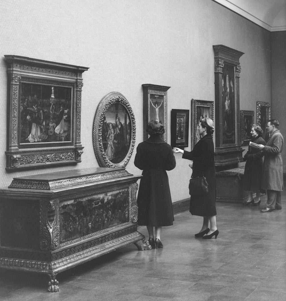 a black and white photo of people looking at paintings