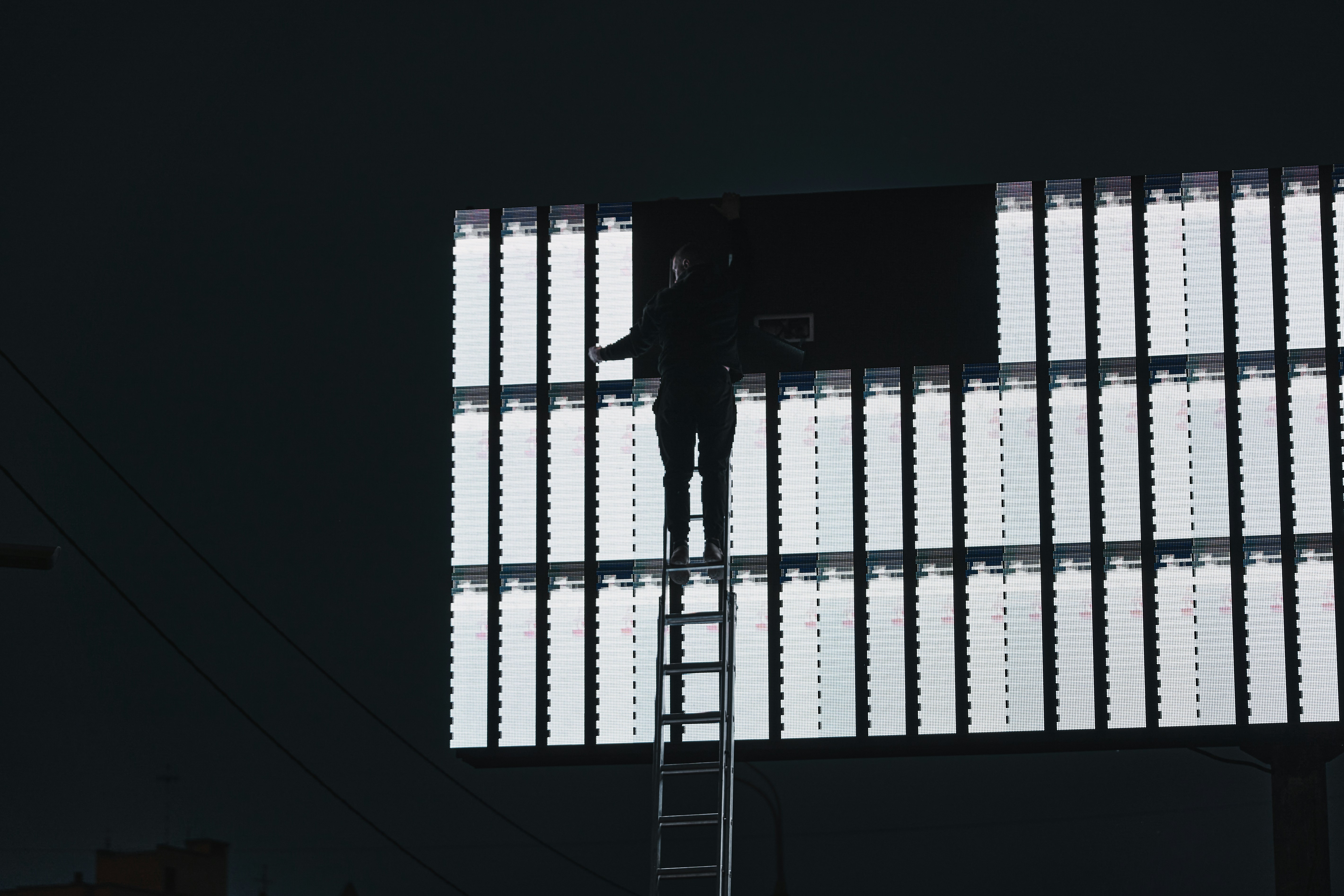 A man on a ladder working on a large screen