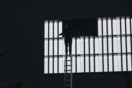 Technician carefully mounting a large vinyl banner on an outdoor billboard frame.