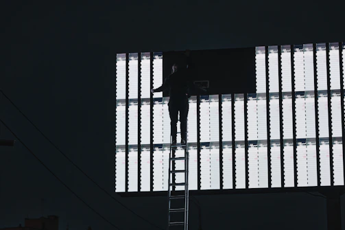 Technician adjusting a large LED billboard on a rooftop overlooking the cityscape of Calama.