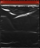 A transparent plastic zipper storage bag with a red and yellow sealing stripe at the top. The bag appears shiny under light, showing reflections and creases in the material.