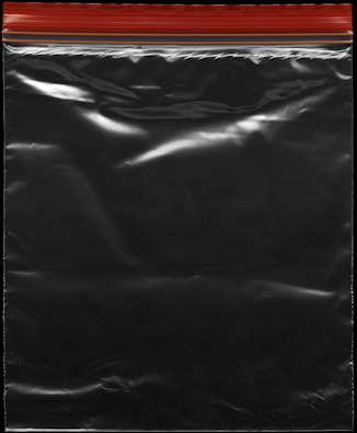 A transparent plastic zipper storage bag with a red and yellow sealing stripe at the top. The bag appears shiny under light, showing reflections and creases in the material.
