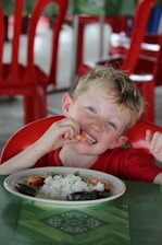 A calm child smiling while eating rice with a gentle therapist nearby