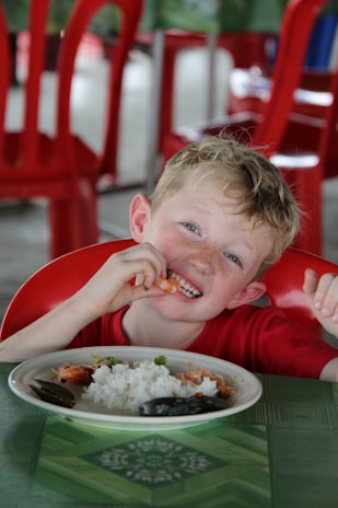 Photo of a calm child happily sitting at the table with a bowl of rice, showing comfort and trust.