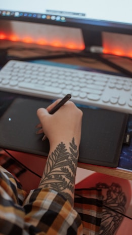 An intimate close-up of hands working on a graphic design tablet, illuminated by a soft red light.