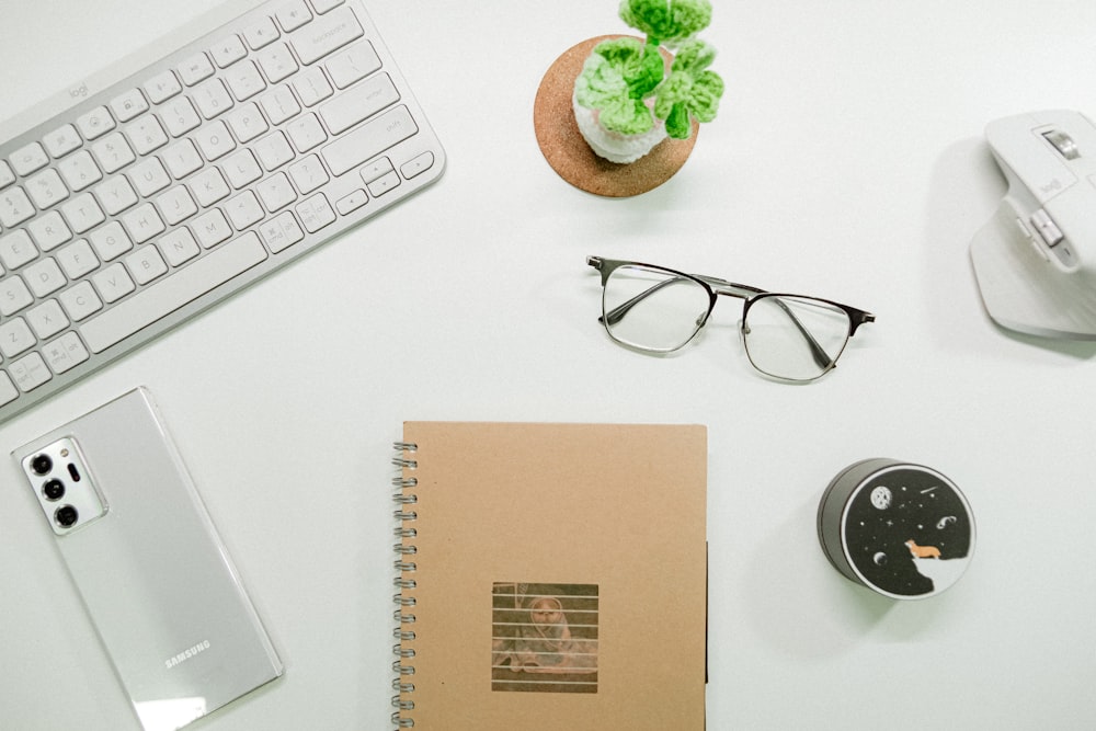 a desk with a keyboard, mouse, cell phone and a notepad