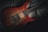A beautifully crafted electric guitar with a rich mahogany finish and intricate wood grain patterns is seen resting against a dark fabric background. The guitar's body features shiny black pickups and a set of six strings extending across the fretboard.