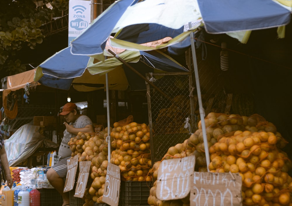 a fruit stand with lots of oranges under a blue umbrella