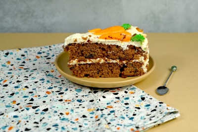 A plate featuring a freshly baked carrot cake slice with a sprig of mint.