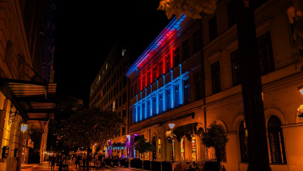 a city street at night with buildings lit up in red, white and blue