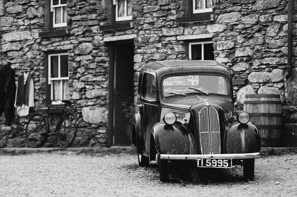 a black and white photo of an old car parked in front of a stone building