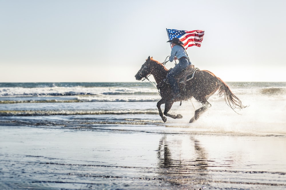 Uma pessoa montando um cavalo com uma bandeira americana nas costas
