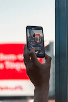A close-up of a woman’s hand holding a smartphone with Brazilian landmarks blurred in the background.