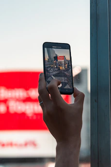 A close-up of a citizen holding a smartphone, reporting an issue on the Corrupción Tlalpan platform, with urban buildings blurred in the background.