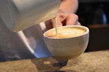 Barista pouring latte art into a ceramic cup at a coffee counter.