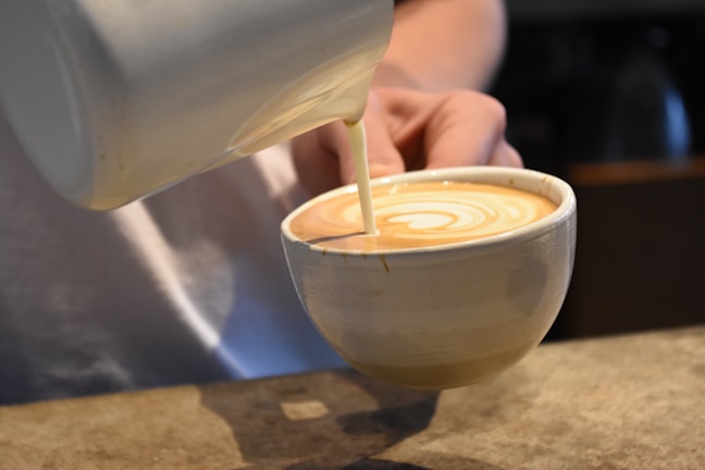 Barista pouring latte art into a ceramic cup at a coffee counter.