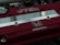 A close-up view of a car engine cover featuring the red and silver branding of a Honda DOHC VTEC engine. The cover has a metallic Honda logo and several screws visible.