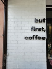 a white brick wall with a sign that says, but first, coffee