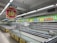 A nearly empty supermarket with empty shelves and freezer units. Colorful signs advertise discounts of up to 80% and other promotional offers in bold fonts above the shelves. The image conveys a sense of clearance sale or store closure.