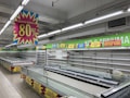 A nearly empty supermarket with empty shelves and freezer units. Colorful signs advertise discounts of up to 80% and other promotional offers in bold fonts above the shelves. The image conveys a sense of clearance sale or store closure.