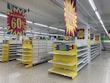 Empty supermarket shelves are surrounded by bright sale signs displaying discounts up to 60%. The banners are in bold colors, with phrases indicating a significant stock clearance. The store appears vacant, with no products on the shelves and no people present.